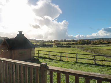 A wooden structure with a fenced green field and rolling hills in the background at Sunnyside Lodge in Crewkerne