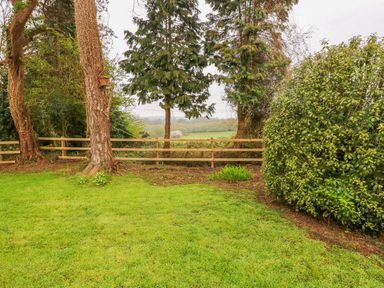 A garden with grass trees bushes a wooden fence and a field in the background at 4 Hanbury Lodge in Pentlepoir