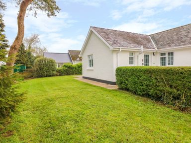 A white building with a tiled roof and green hedges surrounded by grass at 4 Hanbury Lodge in Pentlepoir