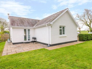 An exterior view of a white house with a tiled patio and grass lawn at 4 Hanbury Lodge in Pentlepoir