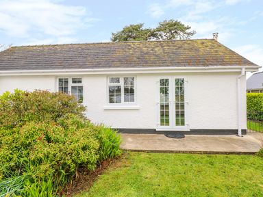 A white exterior wall with two windows and glass double doors next to a garden with shrubs at 4 Hanbury Lodge in Pentlepoir