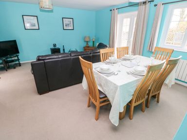 A dining table set with plates and glasses next to a black sofa in a living room with blue walls at 4 Hanbury Lodge in Pentlepoir