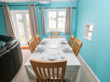 A dining room with a wooden table set for six and light blue walls at 4 Hanbury Lodge in Pentlepoir