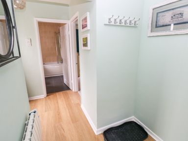 A hallway with light wood flooring a radiator a black mirror hooks on the wall and an open door leading to a bathroom at 4 Hanbury Lodge in Pentlepoir