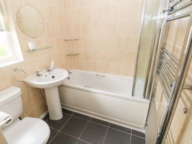 A bathroom with a bathtub sink toilet round mirror and heated towel rail at 4 Hanbury Lodge Pentlepoir
