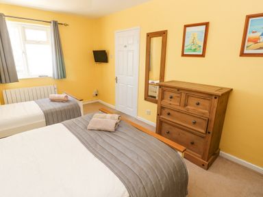 A bedroom with two single beds a wooden chest of drawers a wall mirror and a window with curtains at 4 Hanbury Lodge in Pentlepoir