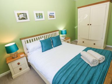 A bedroom with a double bed two bedside tables with lamps a wardrobe and three framed pictures on a green wall at 4 Hanbury Lodge in Pentlepoir