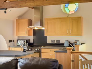 A kitchen with wooden cabinets a black countertop a stove a kettle and a bottle with glasses on the counter at Moor View Chapel in Camelford