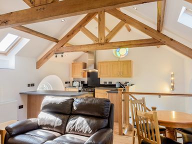 An open plan kitchen and dining area with wooden beams a leather sofa and skylights at Moor View Chapel in Camelford