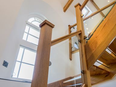A wooden staircase with glass panels next to a large window in a white room at Moor View Chapel in Camelford