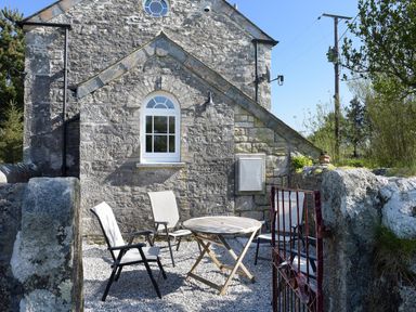 An outdoor seating area with four chairs and a round table on gravel outside a stone building at Moor View Chapel in Camelford