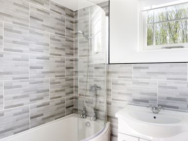 A bathroom with a bathtub shower combination and a sink under a window at Moor View Chapel in Camelford