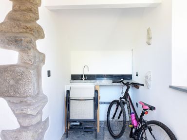 A small utility area with a stone sink countertop, folded chairs, and a bicycle at Moor View Chapel in Camelford
