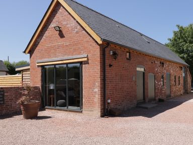 A brick building with a sloped roof and large sliding glass door at The Stables in Cross Keys near Hereford