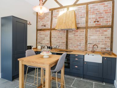 A kitchen with a wooden table and two chairs and blue cabinets against a brick wall at The Stables in Cross Keys near Hereford
