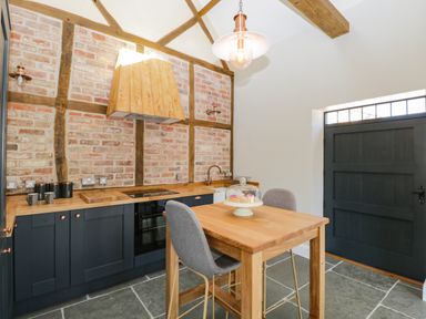 A kitchen with wooden countertops brick and beam walls a small wooden dining table with two grey chairs and a dark door at The Stables Cross Keys near Hereford