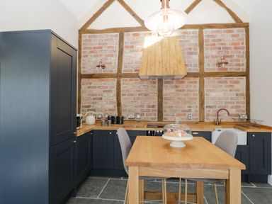 A kitchen with wooden countertops blue cabinets a wooden table with chairs and a brick wall at The Stables in Cross Keys near Hereford