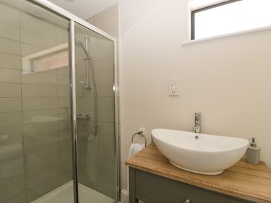 A bathroom with a glass shower enclosure and a white sink on a wooden countertop at The Stables in Cross Keys near Hereford