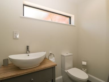 A bathroom with a toilet and a sink on a wooden countertop under a narrow window at The Stables in Cross Keys near Hereford