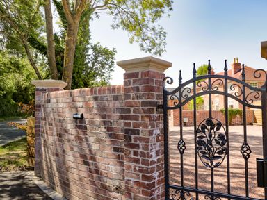 A brick wall with a black wrought iron gate and trees behind at The Stables in Cross Keys near Hereford