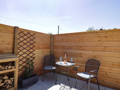 A small outdoor patio with a wooden fence a table two chairs and a planter with a trellis at The Stables in Cross Keys near Hereford