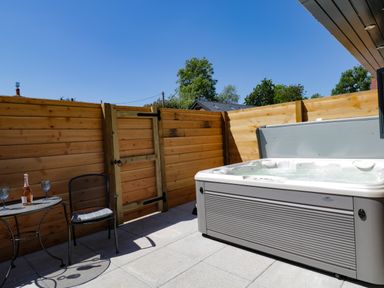 An outdoor patio with a wooden fence a hot tub and a small table with two chairs and glasses at The Stables in Cross Keys near Hereford