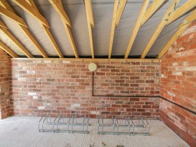 A brick walled room with wooden ceiling beams and two metal bike racks on the concrete floor at The Stables in Cross Keys near Hereford