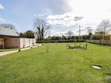 A large green lawn with young trees and a wooden shed under a blue sky at The Stables in Cross Keys near Hereford