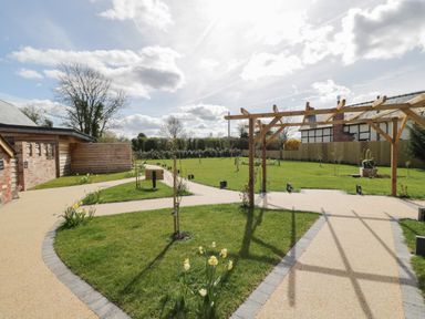 A garden area with pathways trees and a wooden pergola at The Stables in Cross Keys near Hereford