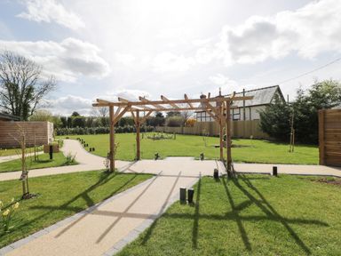 A garden with a wooden pergola over paved paths and grass at The Stables in Cross Keys near Hereford