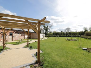 A garden with a wooden pergola and pathways near a brick building at The Stables Cross Keys near Hereford