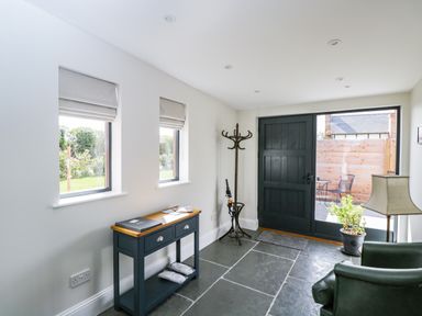 A hallway with two windows and a small table below them next to a coat stand a door and a potted plant at The Stables in Cross Keys near Hereford
