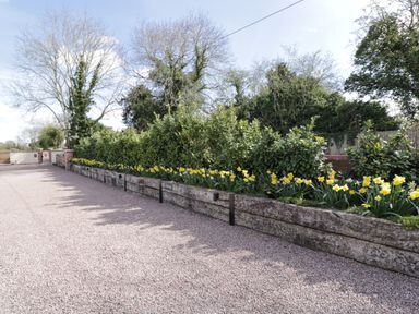 A gravel driveway with raised wooden flower beds containing yellow flowers and green shrubs at The Stables in Cross Keys near Hereford