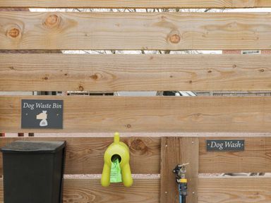 A wooden fence with a dog waste bin black container green dispenser with dog waste bags and a dog wash hose attachment at The Stables in Cross Keys near Hereford