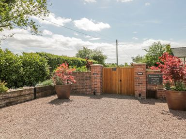 An outdoor entrance with brick walls wooden gate gravel ground and potted plants at The Stables in Cross Keys near Hereford