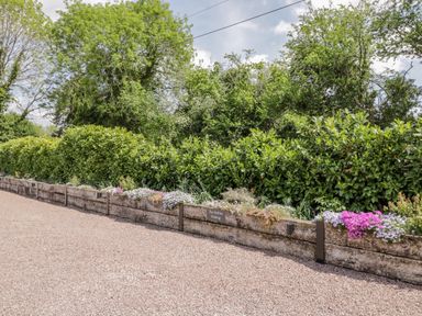 A gravel parking area with wooden planters and green hedges at The Stables in Cross Keys near Hereford