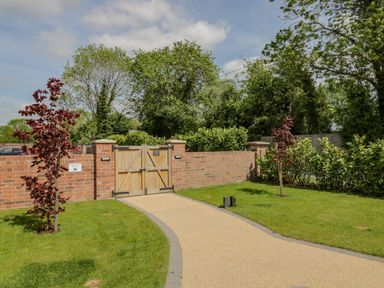 A paved pathway leading to a wooden gate set in a brick wall with trees and shrubs at The Stables in Cross Keys near Hereford