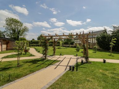 A garden with a wooden pergola and paved pathways surrounded by grass at The Stables in Cross Keys near Hereford