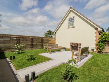 A garden area with two wooden benches a brick barbecue on a paved patio and grass surrounded by a wooden fence at The Stables in Cross Keys near Hereford