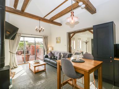 A living and dining area with a black sofa wooden dining table chairs and exposed wooden beams at The Stables in Cross Keys near Hereford