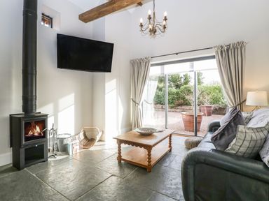 A living room with a wood burning stove television coffee table and leather sofa at The Stables in Cross Keys near Hereford