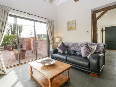 A living room with a black leather sofa and wooden coffee table near a sliding glass door at The Stables in Cross Keys near Hereford