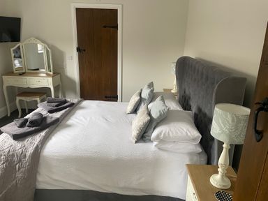 A bedroom with a bed with pillows and towels a dressing table a lamp and a wooden door at The Stables in Cross Keys near Hereford