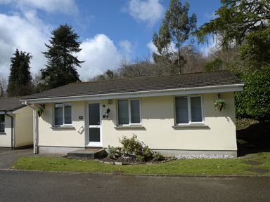 A single story house with a white door and three windows surrounded by trees at Little Retreat in Liskeard