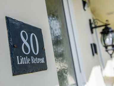 A close up of a house number sign 80 Little Retreat on a wall with a door and lantern in Liskeard