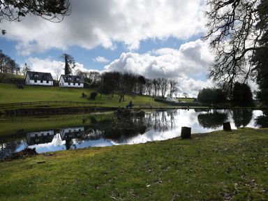 A pond with reflections of houses trees and clouds on a grassy area at Little Retreat in Liskeard