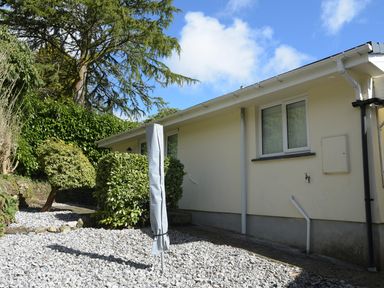 A garden area with gravel ground and trimmed bushes next to a single-story building with windows at Little Retreat in Liskeard
