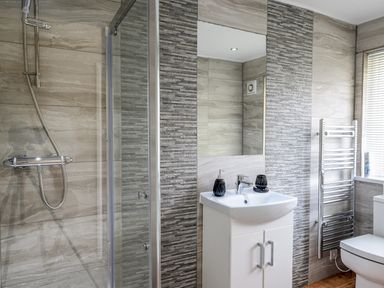 A bathroom with a shower, sink with cabinet, mirror, towel rack, and toilet at Little Retreat in Liskeard