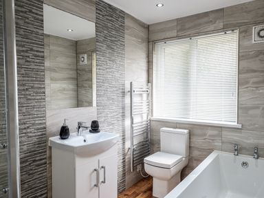 A bathroom with a sink cabinet a toilet a bathtub and a window with blinds at Little Retreat in Liskeard