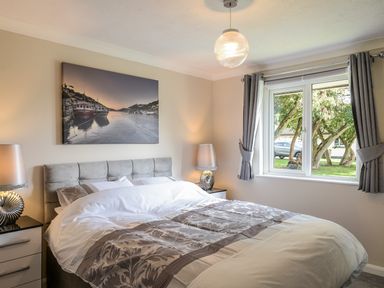 A bedroom with a bed lamps bedside tables a window with gray curtains and a wall picture at Little Retreat in Liskeard